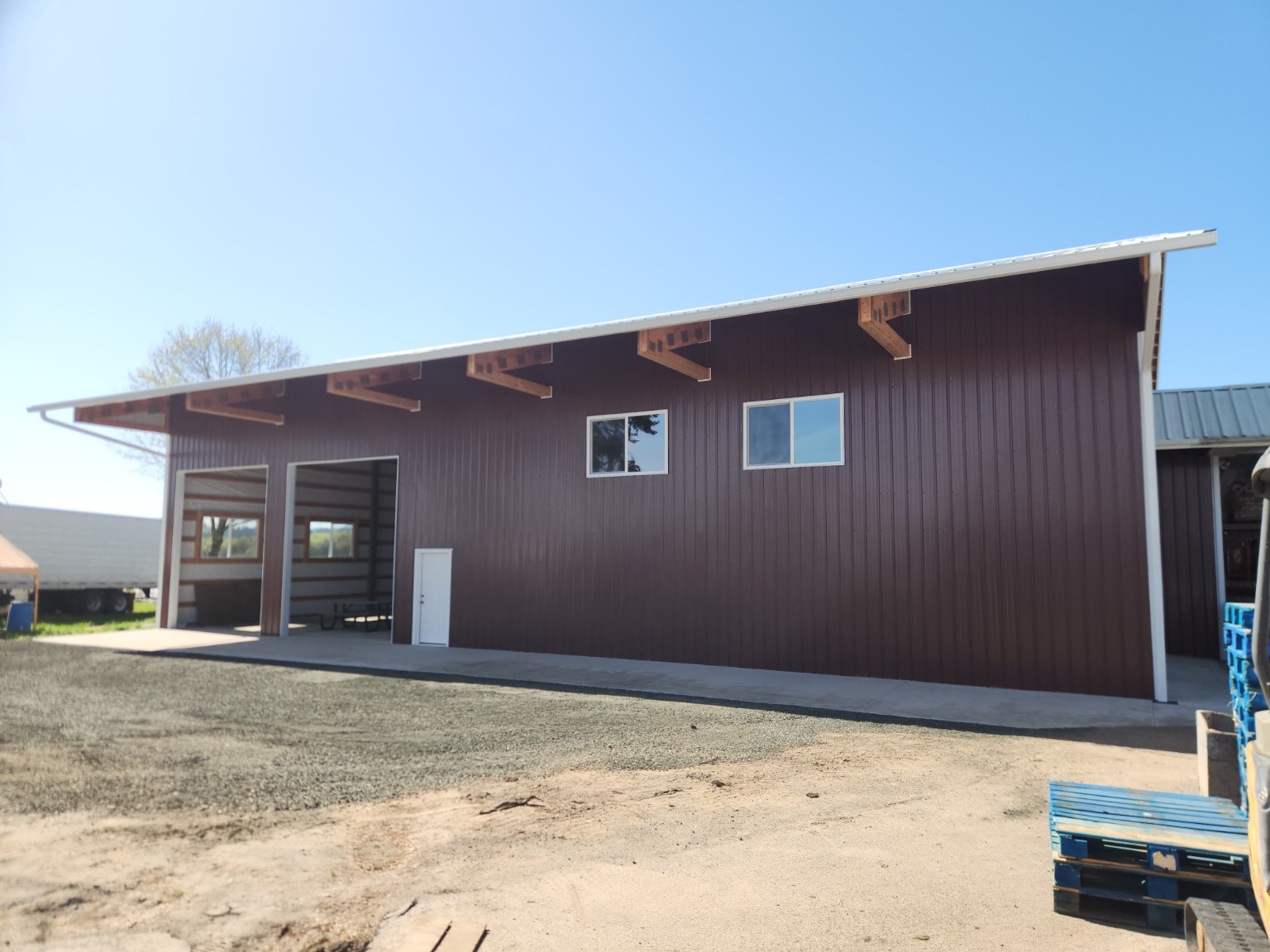 Long dark red post-frame shop with open bays and windows